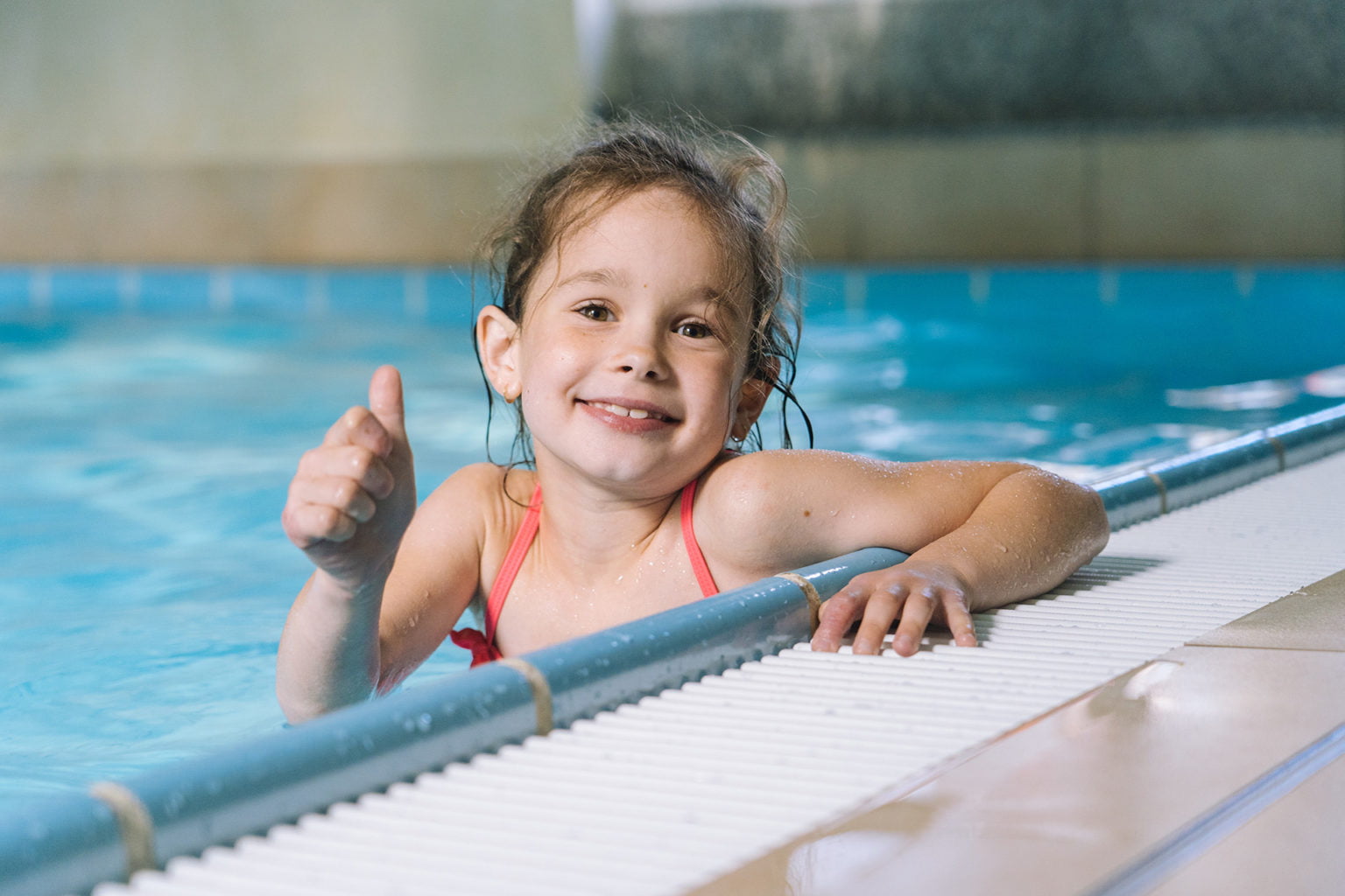 Portrait little girl having fun in indoor swimming-pool. The girl is resting at the water park. Active happy kid. Swimming school for small children. Concept friendly family sport and summer vacation.