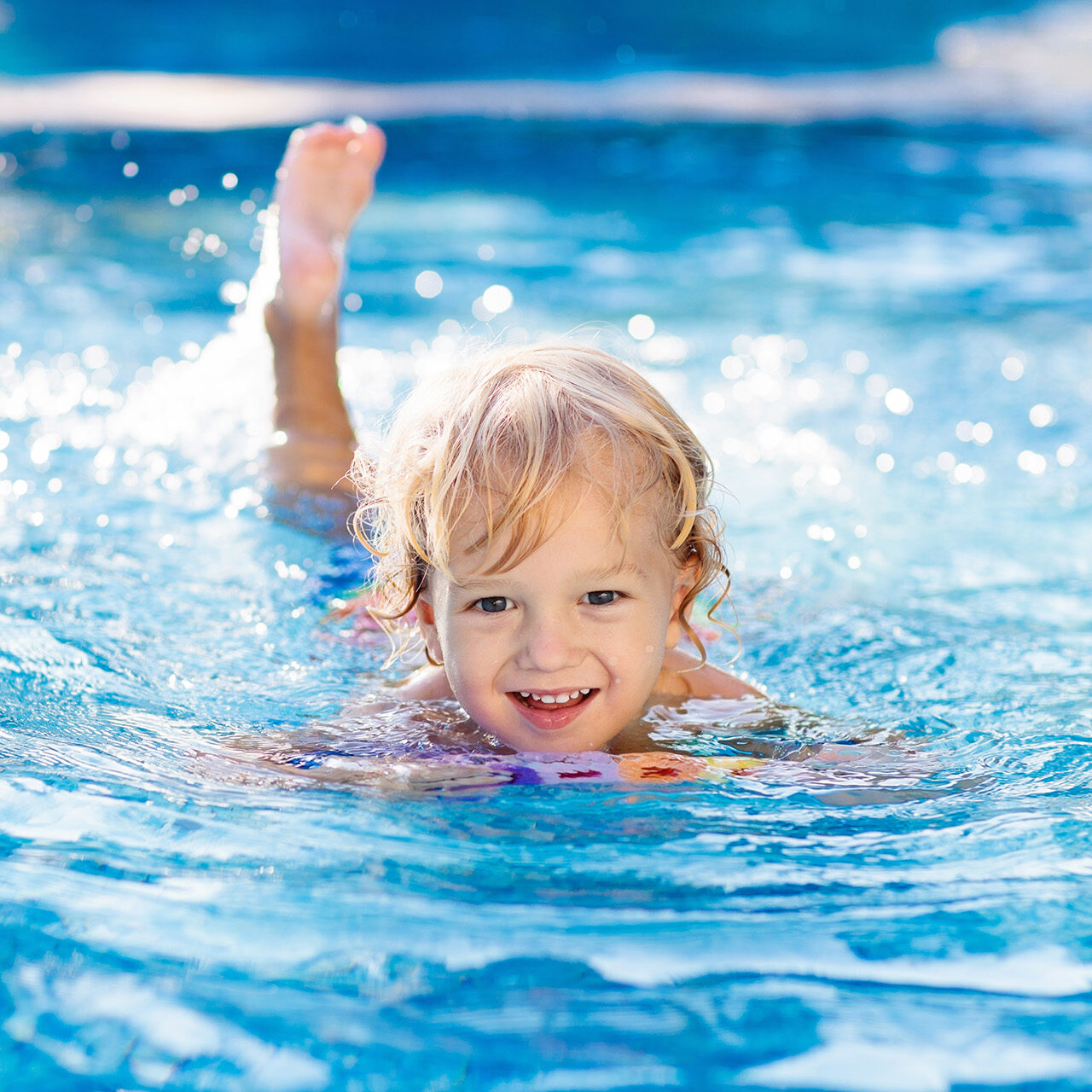 Child learning to swim in outdoor pool of tropical resort. Kids learn swimming. Exercise and training for young children. Little boy with colorful float board in sport club. Swimming baby or toddler.